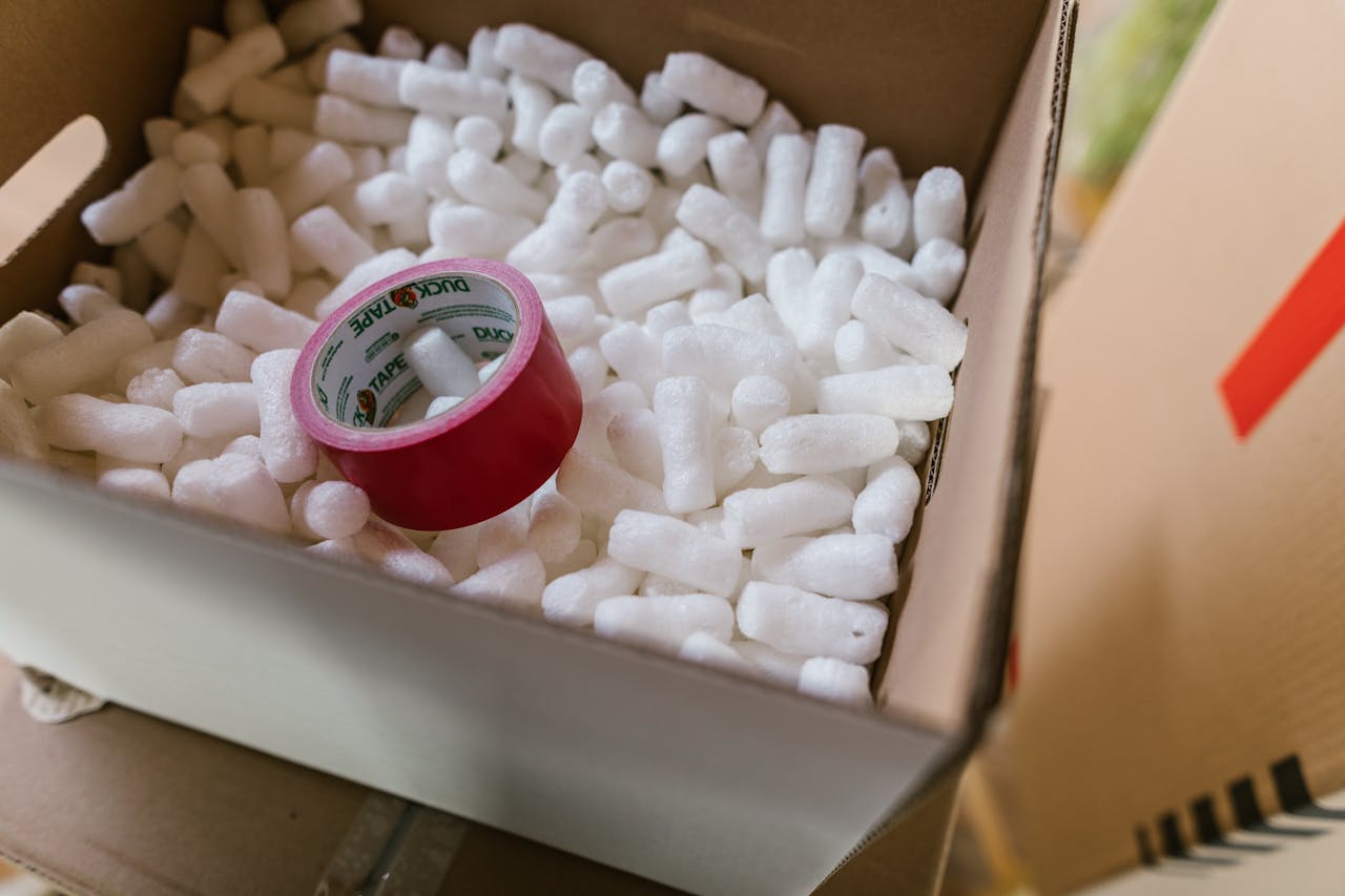 Close-up of a cardboard box filled with packing peanuts and red tape.